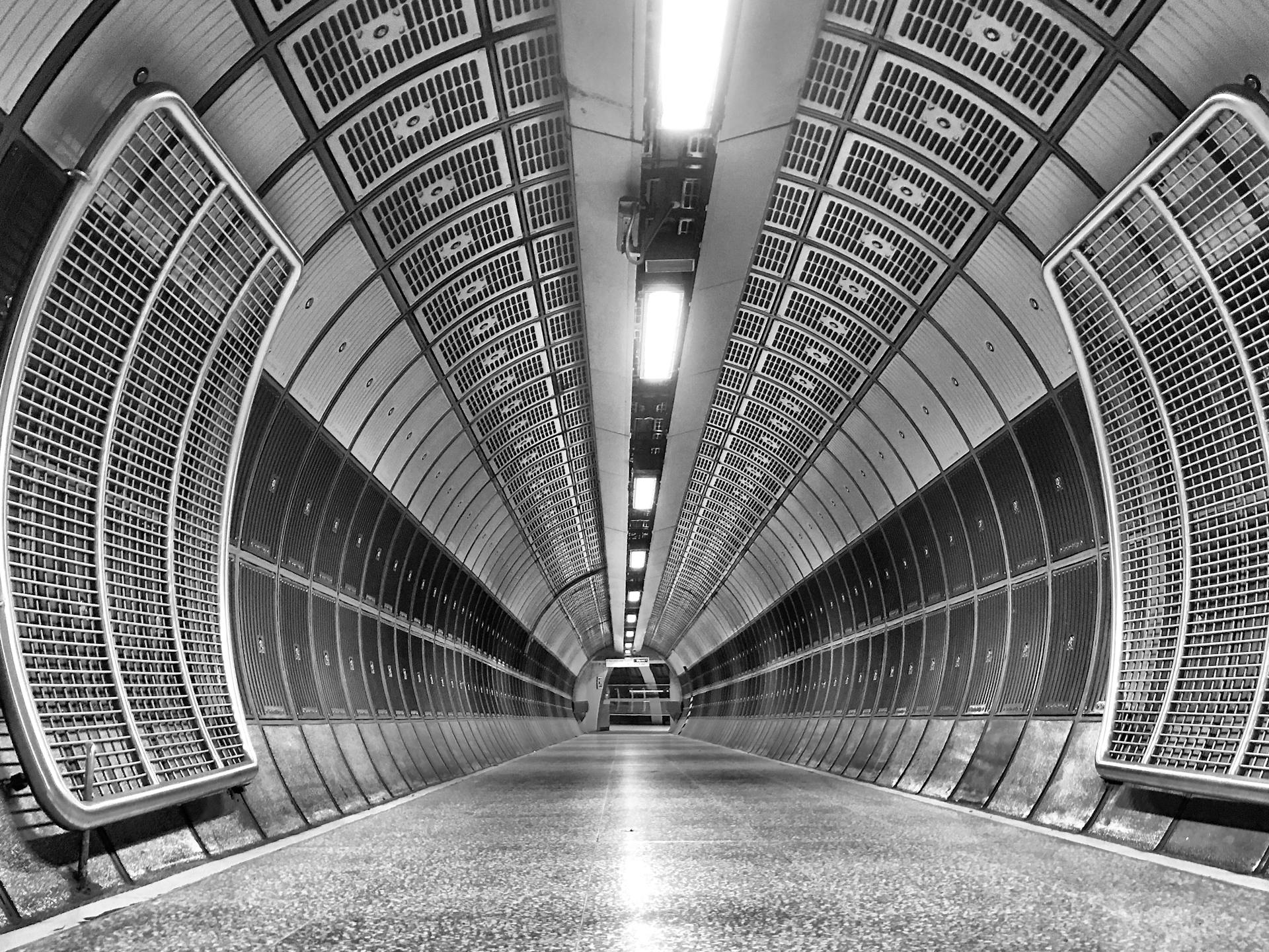 A dramatic black and white view of an empty tunnel in a London underground station.