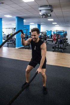 Adult man working out with battle ropes in a modern gym setting, focused on fitness and wellness.