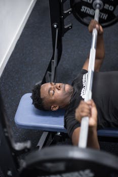 African American man lifting a barbell on a bench press indoors, emphasizing strength and focus.