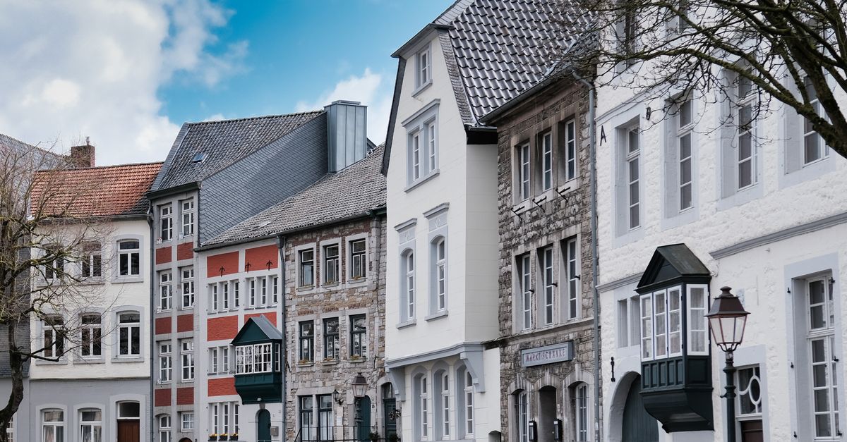 Historische Hausfassaden säumen eine alte Straße in Aachen unter blauem Himmel