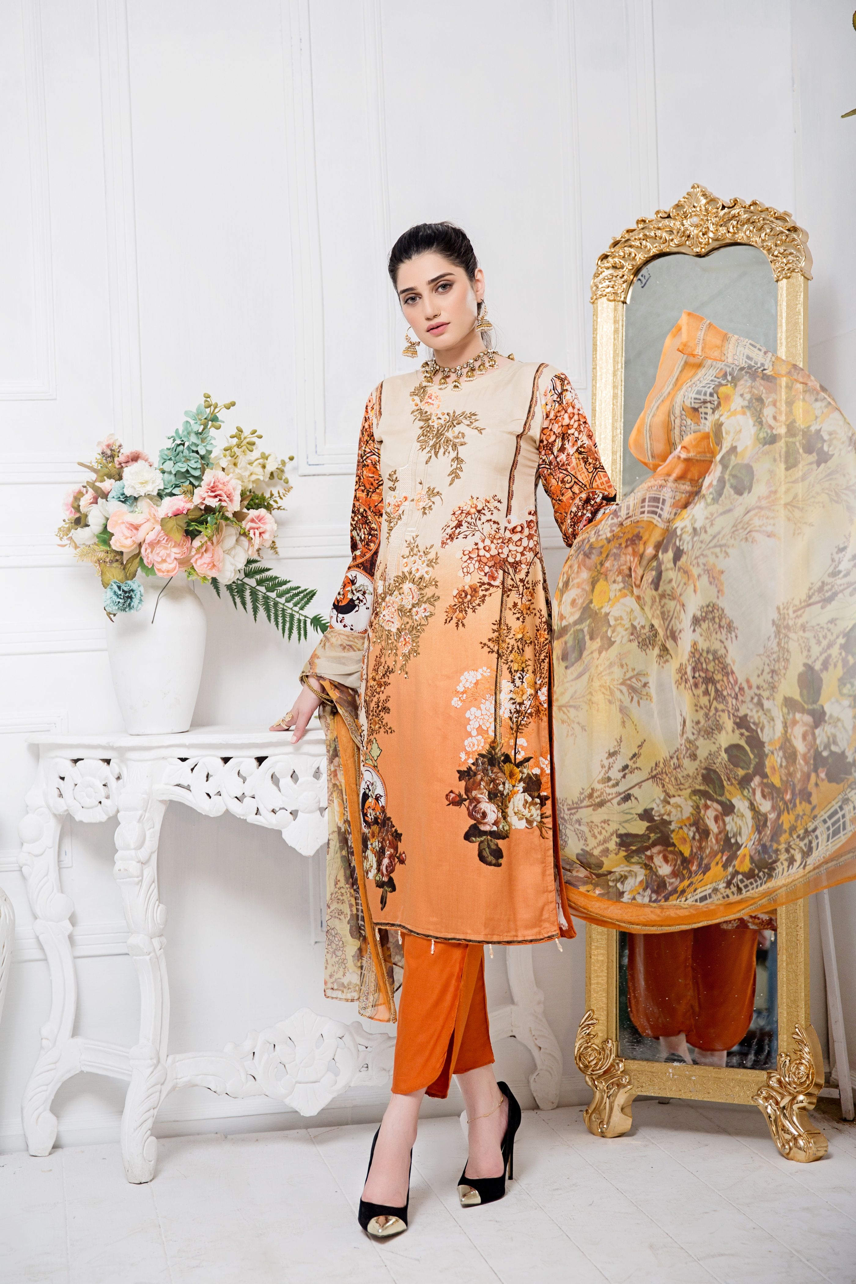 Indian woman posing in traditional orange floral dress with dupatta indoors.