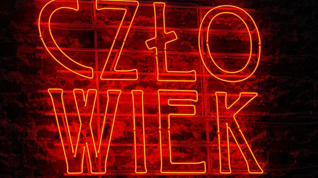Glowing red neon sign reading 'CZŁOWIEK' on a dark brick wall, striking and bold.
