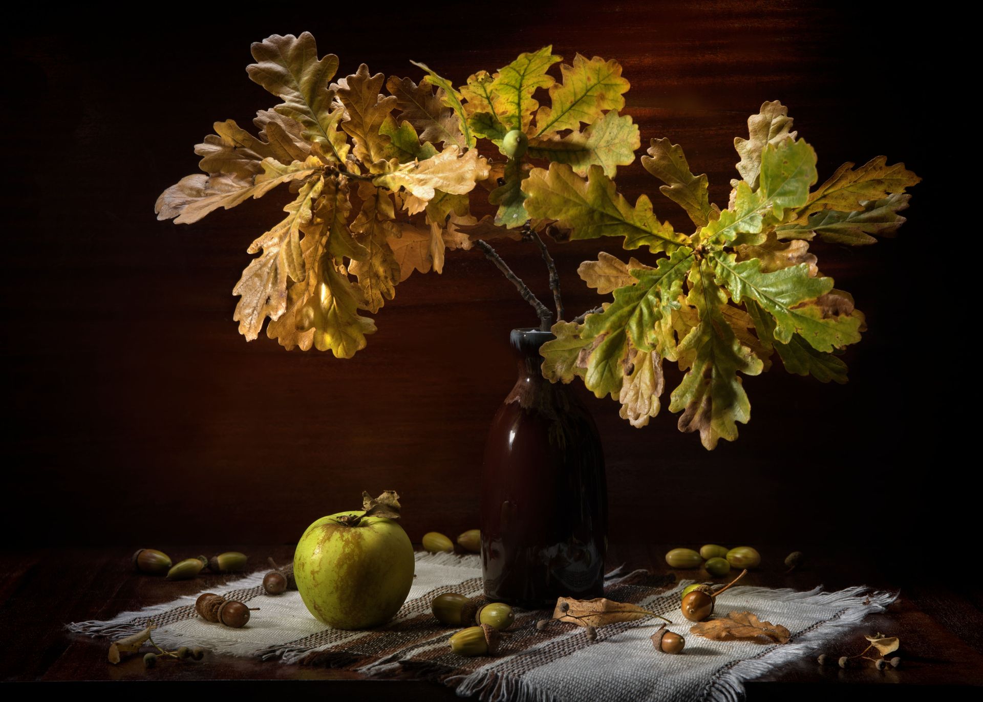 Artistic composition featuring oak leaves, acorns, and an apple with autumn tones.