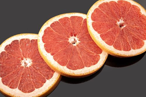 Free Vibrantly colored grapefruit slices artistically arranged against a sleek black surface. Stock Photo