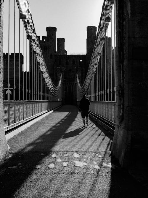 A Grayscale Photo of a Person Walking on a Bridge