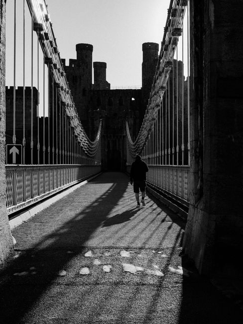 A person walking on the historic Conwy Suspension Bridge in Wales, captured in striking black and white.