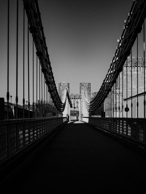 A striking black and white image of the historic Conwy Suspension Bridge in Wales, capturing its dramatic architecture.