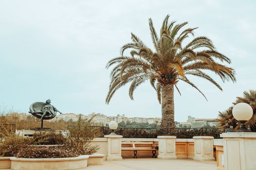 An elegant terrace with a palm tree and sculpture under a clear sky.