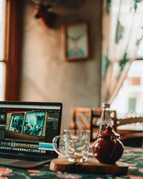 Modern netbook placed on table near wooden stand with glass cup and teapot with hot beverage in cafeteria on blurred background