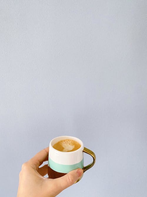 Female hand with ceramic mug of aromatic freshly brewed cappuccino with froth on gray background