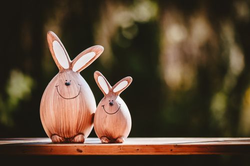 Free Two adorable wooden bunny figurines with happy faces on a table against a blurred outdoor background. Stock Photo
