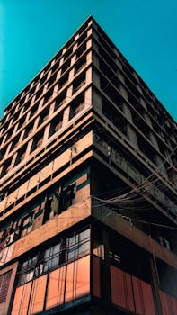 一座高大的现代建筑在晴朗蓝天下呈现低角度视角，玻璃窗清晰可见