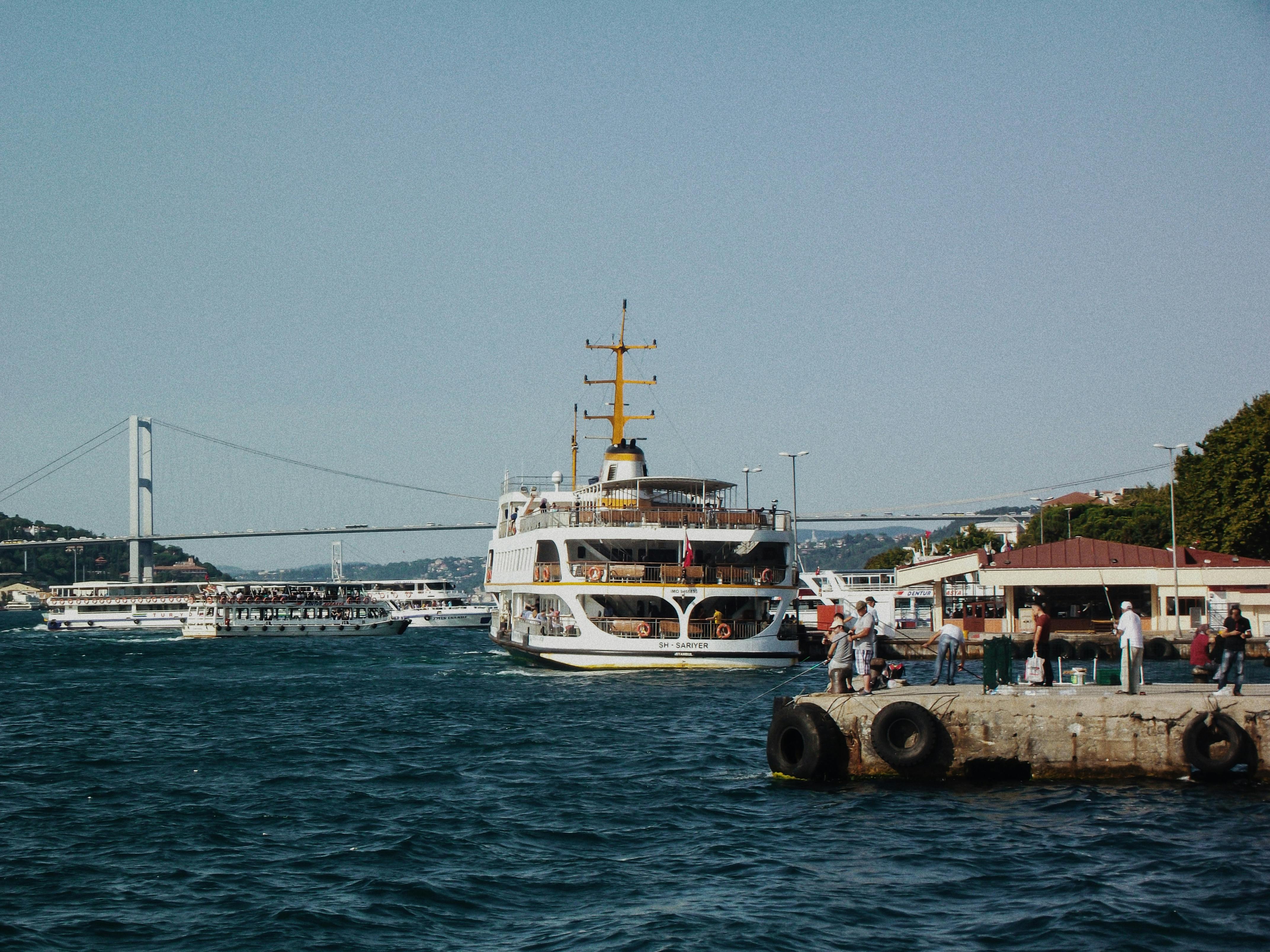 Free Ferry and people at a bustling dock in Istanbul, with the Bosphorus Bridge in the background. Stock Photo