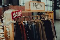 Assorted modern clothing hanging on hangers on rack with Sale inscription in spacious shop with dressing rooms and various accessories