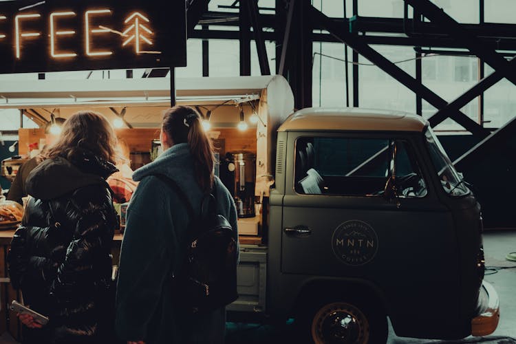 Women Choosing Coffee Near Van With Sparkling Lights