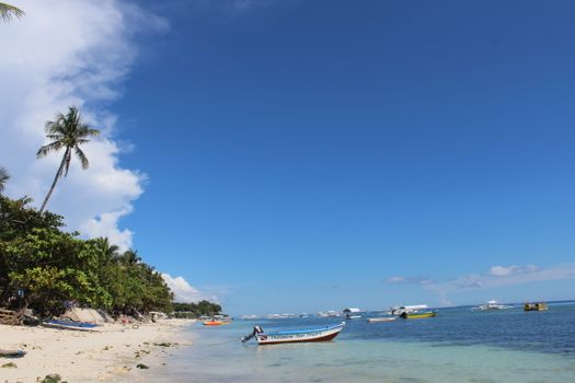 Scenic view of Panglao's picturesque beach with boats and palm trees under a blue sky.