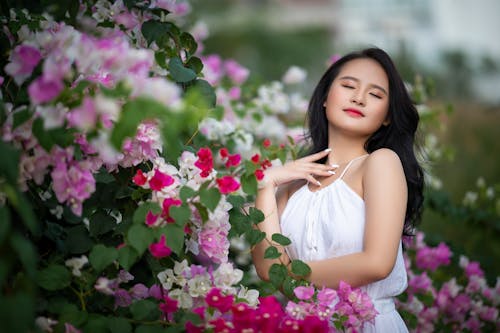 Free Young Asian woman standing in blooming garden with flowers Stock Photo
