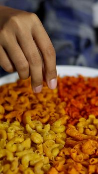 A close-up of a hand seasoning a colorful macaroni dish with vibrant spices.