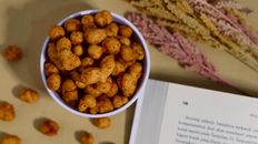 Overhead view of crunchy snacks in a bowl with an open book and dried flowers.