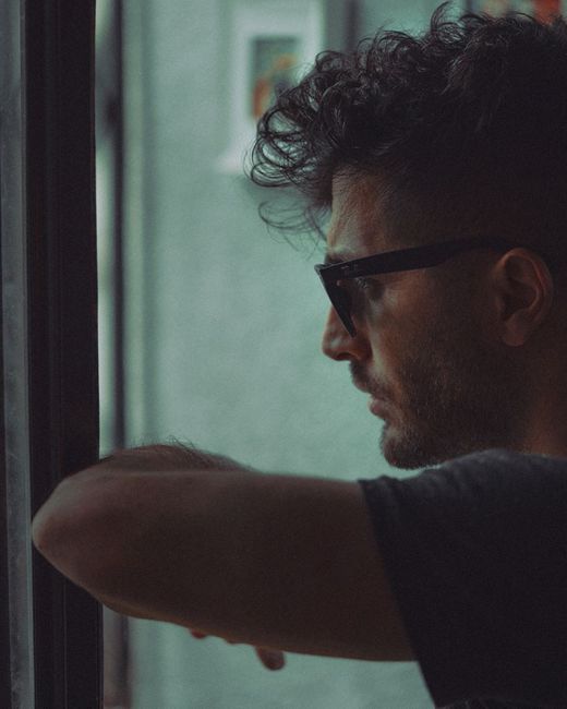 Close-up side profile of a man wearing sunglasses, thoughtfully gazing out a window.