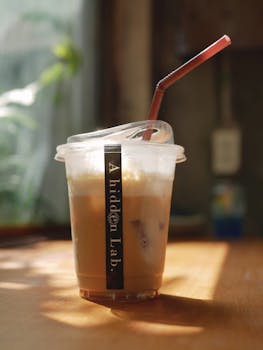 A close-up of a refreshing iced coffee in a disposable cup with a straw on a sunny café table.