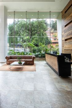 Spacious modern office lobby featuring a leather sofa and glass wall overlooking lush greenery.