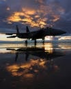一架军用喷气式飞机停在潮湿的停机坪上，倒映着引人注目的日落，展现出充满活力的天空