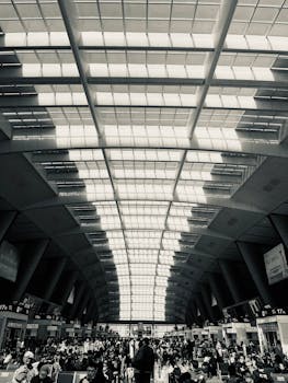 Black and white photo capturing a crowded, modern airport terminal with a striking glass ceiling.