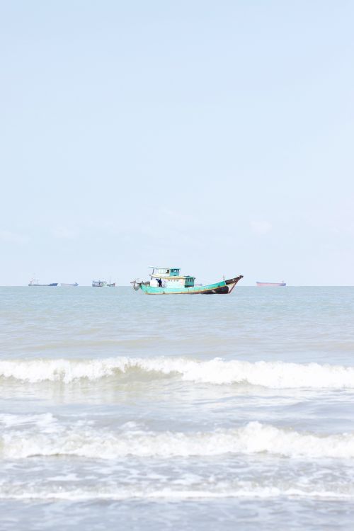 Free A tranquil scene of a fishing boat on a calm ocean with gentle waves under a clear sky. Stock Photo