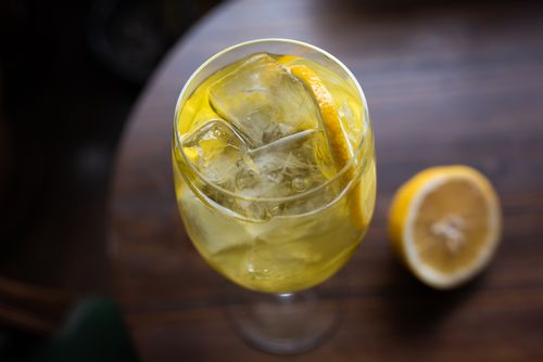 Free Chilled citrus beverage in a wine glass with ice cubes and lemon slice on a wooden table. Stock Photo