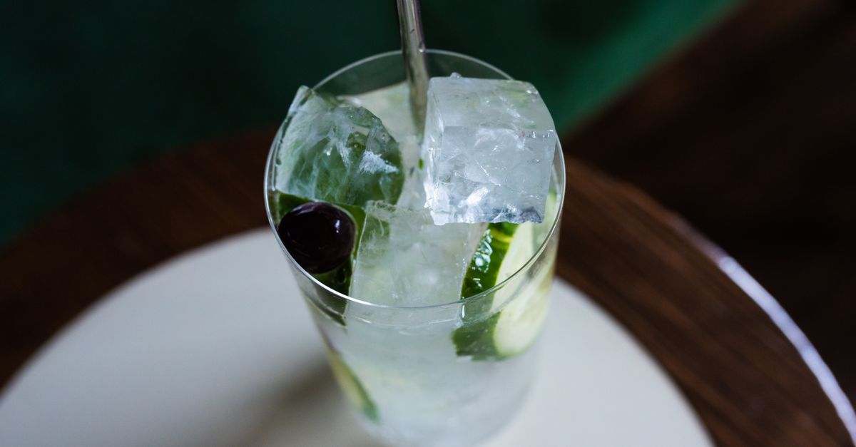Top view of a refreshing gin cocktail with cucumber slices and ice cubes in a clear glass.