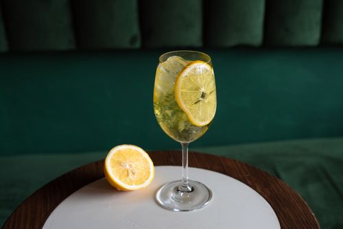 Free A citrusy lemon cocktail with ice in a wine glass on a wooden table, perfect for a refreshing drink. Stock Photo