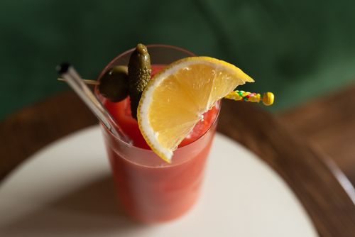 Free Stylish red cocktail served with lemon slice, pickles, and glass straw. Perfect for summer refreshment. Stock Photo