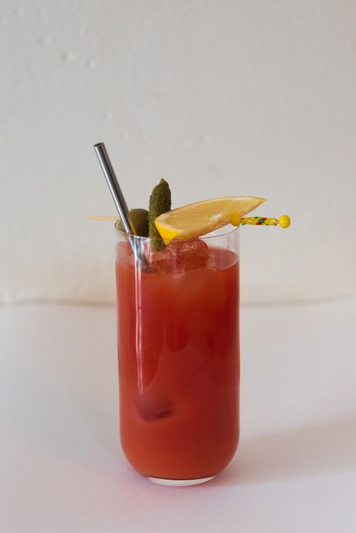 Free Red cocktail with ice, lemon slice, pickles, and a stainless steel straw on a white surface. Stock Photo