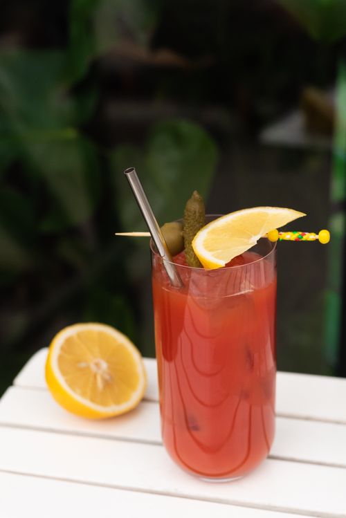 Free Vibrant red cocktail with lemon slice and pickle garnish, set on a white table outdoors. Stock Photo
