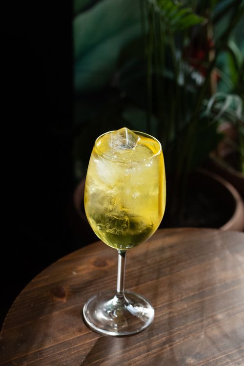 Free A refreshing yellow cocktail with ice served in a wine glass on a wooden table, perfect for a sophisticated setting. Stock Photo
