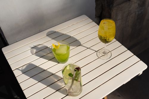 Free Three vibrant cocktails with garnishes on a sunlit white wooden table. Stock Photo
