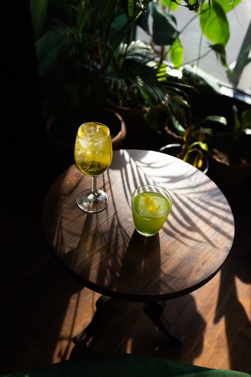 Free Two refreshing green cocktails placed on a rustic table surrounded by indoor plants and natural light. Stock Photo