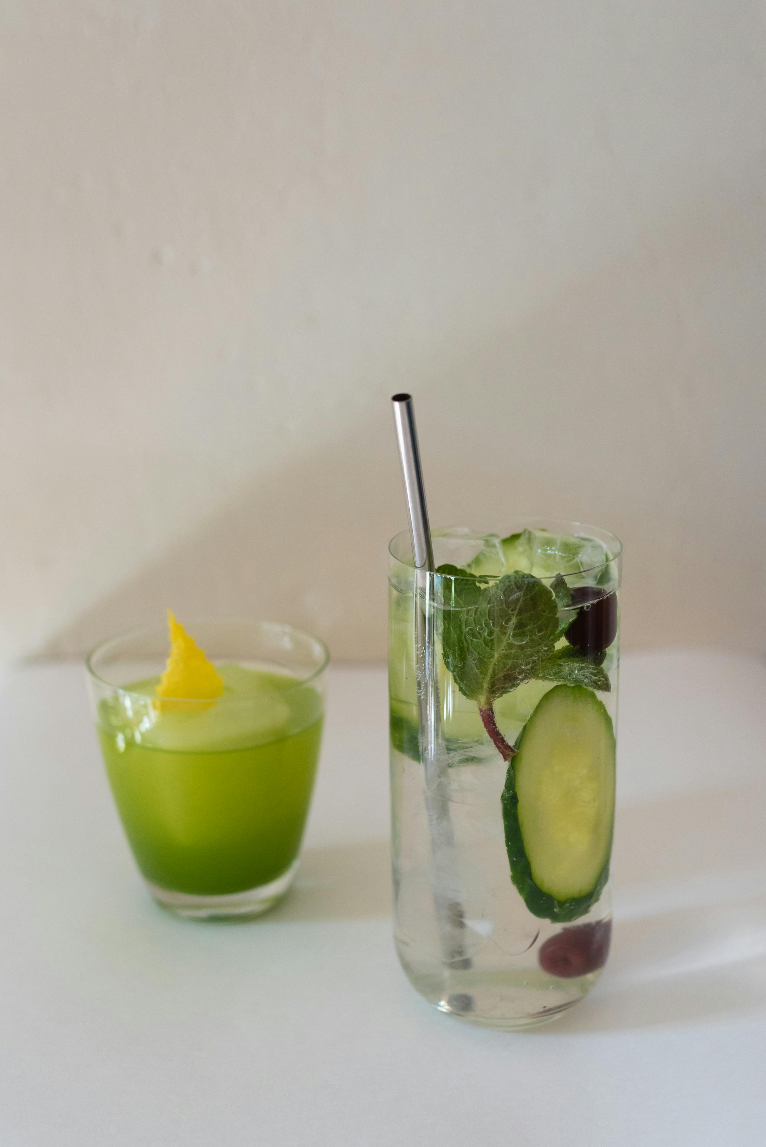 Elegant cocktail with cucumber and mint alongside a green juice. Perfect for refreshing moments.