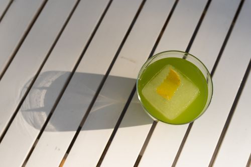 Free Top-down view of a green cocktail with a lemon twist on a sunny striped surface. Stock Photo