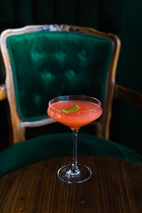 Free A vibrant cocktail garnished with lime sits on a wooden table with a plush chair backdrop. Stock Photo