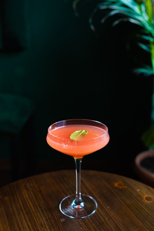 Free A vibrant cocktail in a coupe glass with a lime garnish on a wooden table, perfect for a stylish gathering. Stock Photo