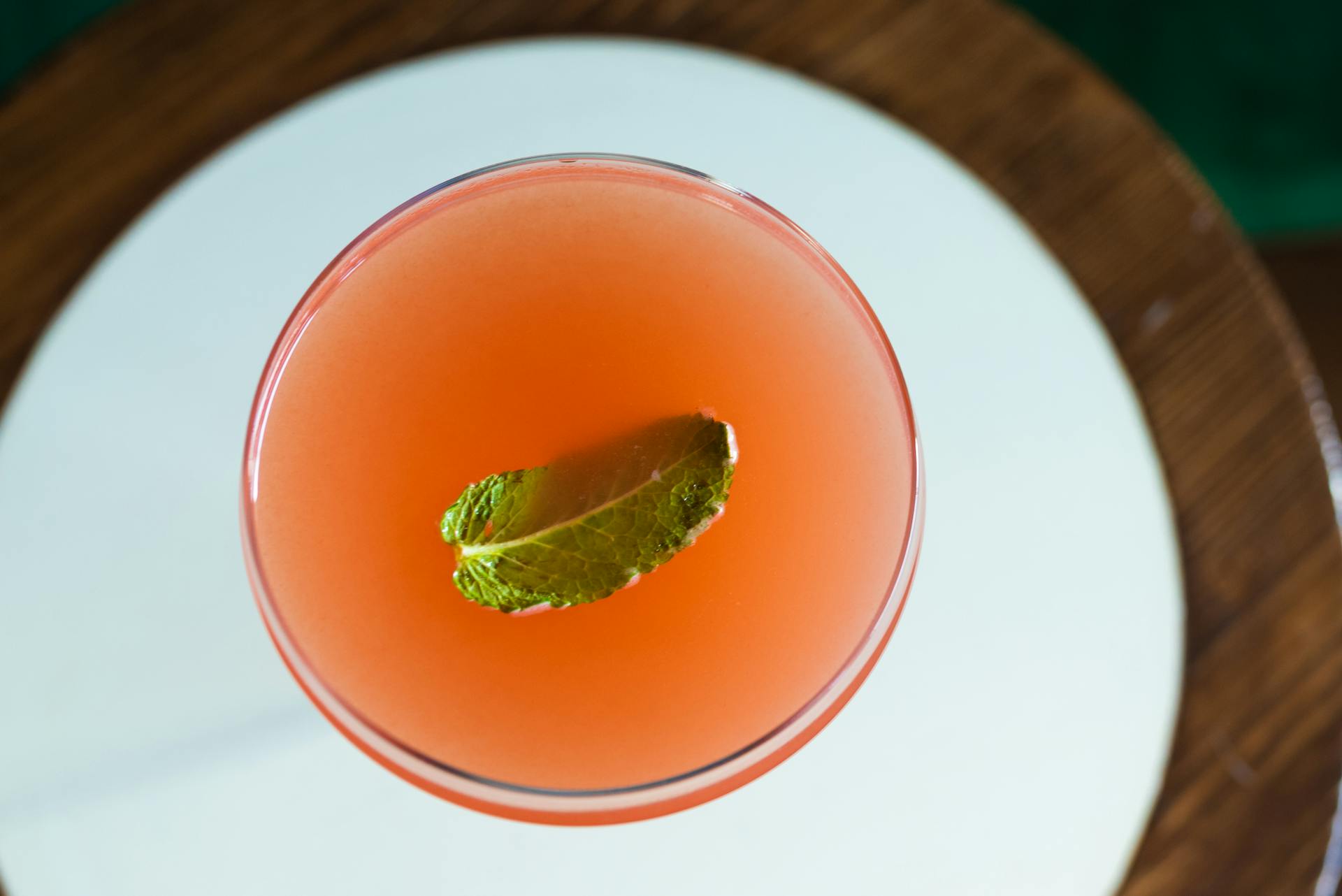 Aerial shot of a vibrant cocktail with mint garnish on a mirrored table.