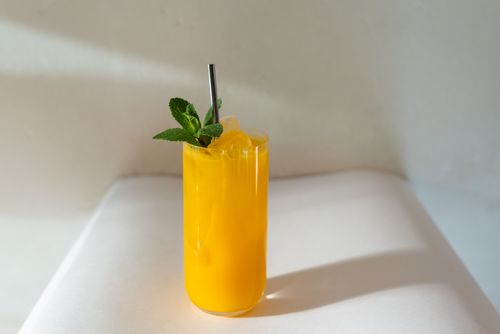 Free Bright yellow mango cocktail served with ice and mint in a glass on a white table. Stock Photo