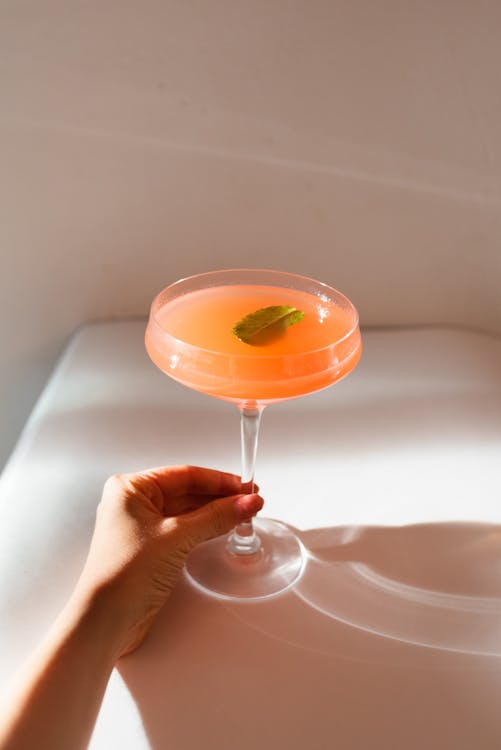 Person Holding Clear Wine Glass With Orange Liquid