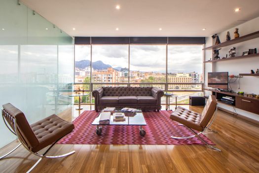 A stylish, minimalist living room featuring large windows, modern furniture, and a cityscape view.