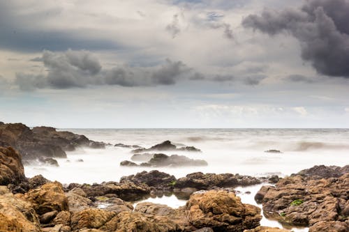 Brown Rocks on Sea Shore Under Cloudy Sky