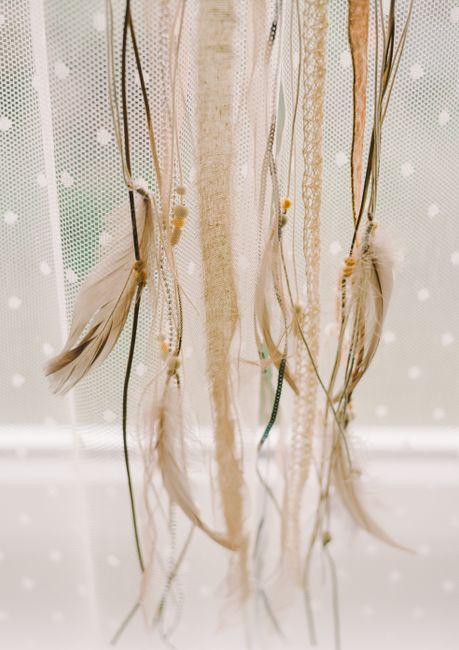 Close-up of a boho dreamcatcher with feathers, lace, and strings hanging decoratively.