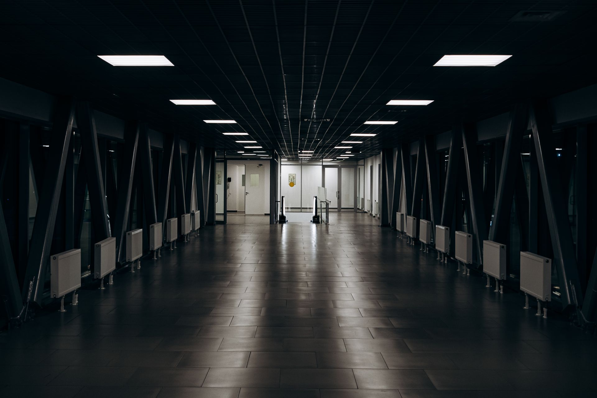 Spacious modern long corridor with clean floor with tile and luminous lamps in darkness