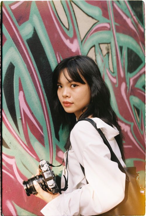 Free Teenage girl holding a camera against colorful graffiti in Ho Chi Minh City. Stock Photo